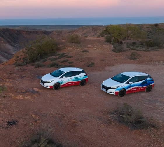 Two Nissan Leaf vehicles with special branding as part of a Horizon Power V2G trial in Exmouth, parked in a red dirt area with a gorge and sunset in the background.