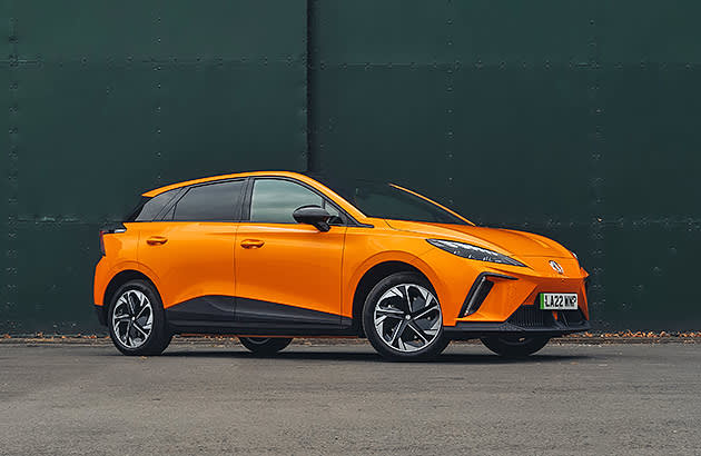 An orange MG4 EV in front of a steel panel