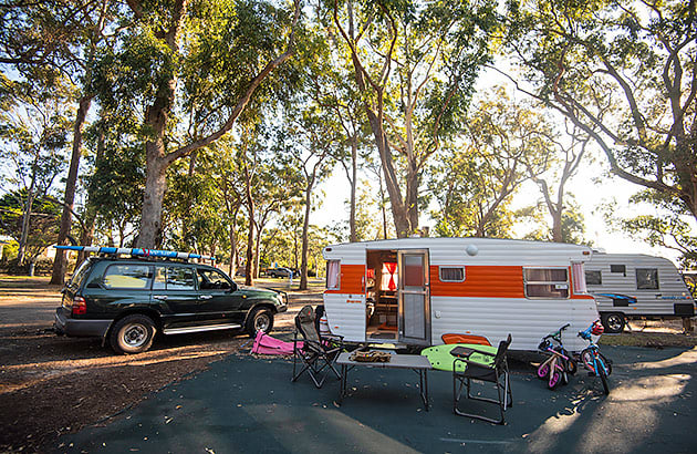 An older style caravan at a caravan park with a 4WD parked near it