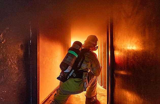 A fire fighter inside a home which in which a fire is blazing