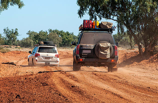 Two four-wheel drives with loaded roof racks on a dirt track