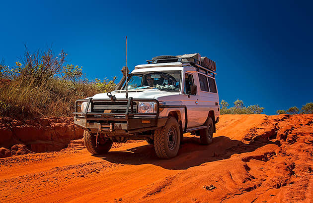 A four-wheel drive with a loaded roof rack on a dirt track