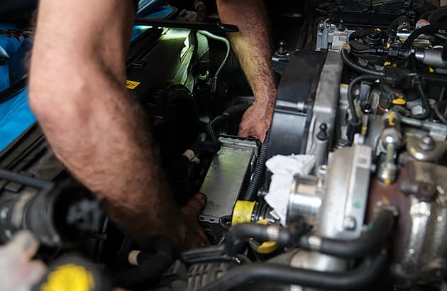 A close up of a person working under a car bonnet