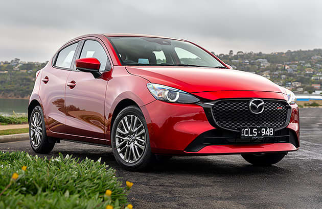 A red Mazda2 parked near a lake