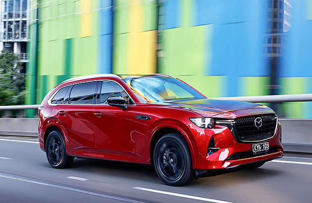 A red Mazda CX-80 driving along a city street