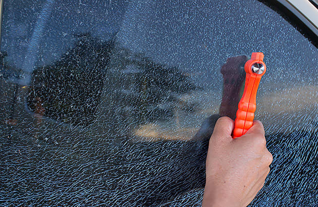 A person is using a glass hammer to smash a car window