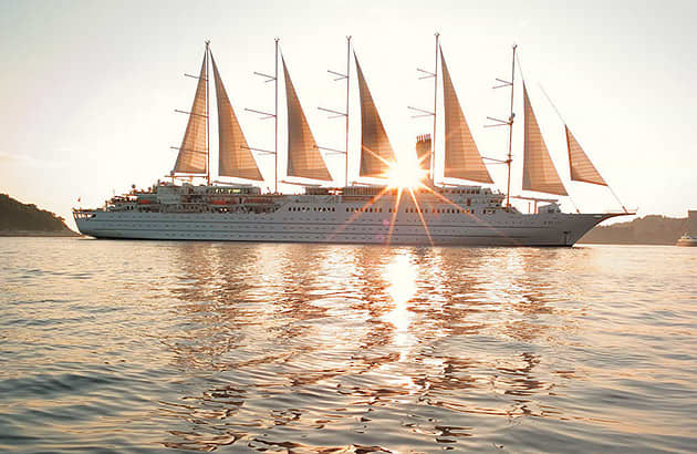 A cruise ship with many sails at sunset seen on the horizon