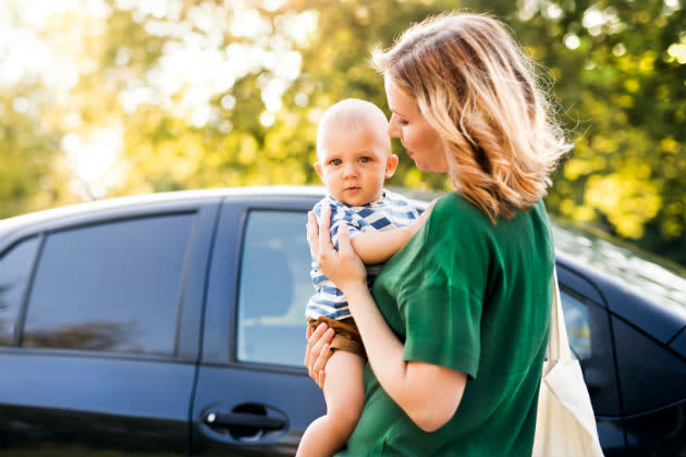 A mother holding her baby next to a black car