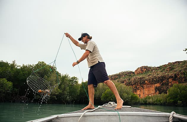 A man is throwing a mud crabbing pot from a small boat