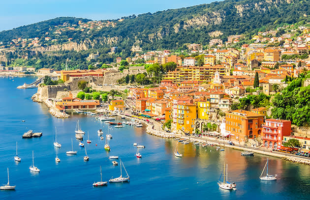 Buildings line the coast of Villefranche sur Mer bay Cote d' Azur France, with many boats moored in the bay close by.