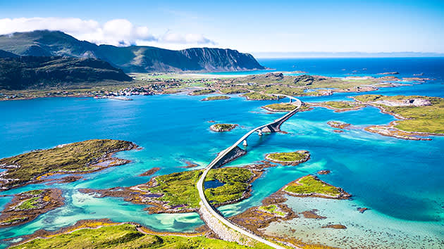 An arial view of the Atlantic Road bridge, which snakes over stunning waterways with mountains in the background in Norway.