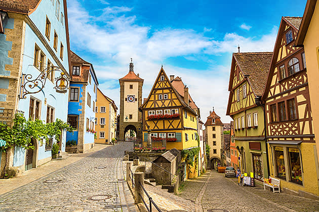 Yellow buildings with pointed wooden rooftops line cobble stone roads in Rothenburg ob der Tauber Germany.