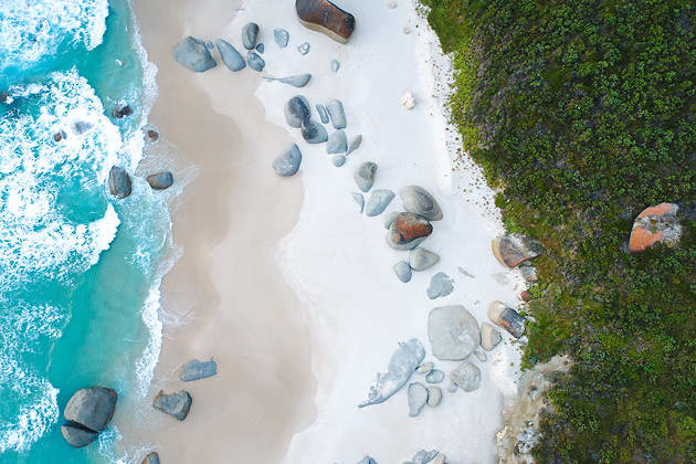 An arial view of a pristine beach in Albany, where large boulders can be seen scattered along the shoreline.