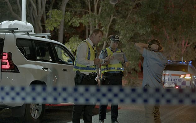 WA Police crash investigation officers conduct interviews at the scene of a road crash, behind a line of police tape.