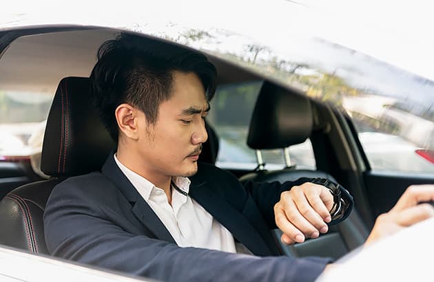 A Thai man in a suit sitting in a car looking at his watch