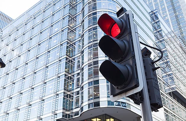A red light at a traffic stop with a tall city building in the background