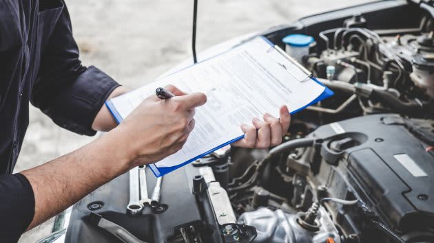 mechanic writing on clipboard in front of car
