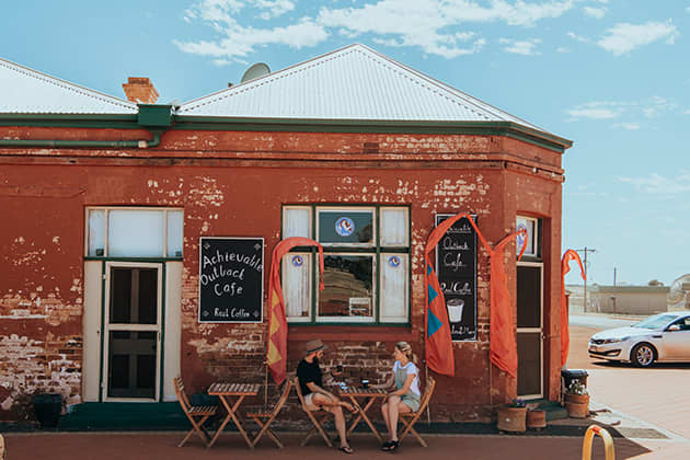 A couple are sitting outside of The Achievable Outback Cafe in Menzies
