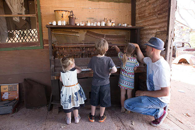 Three children are gathered around a table with an adult watching on.
