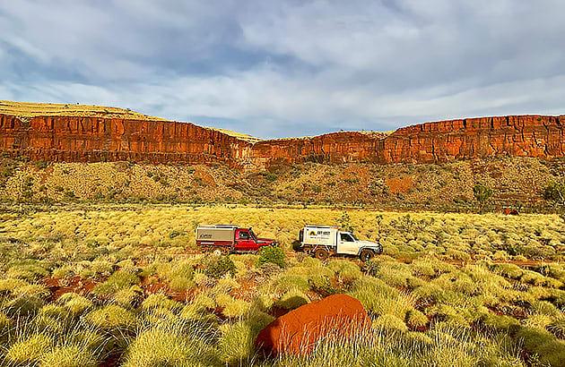 Two four-wheel drives driving along a red dirt track
