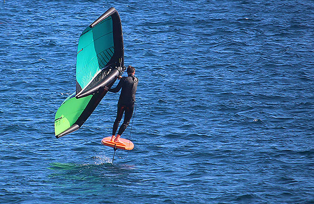 A man wing foiling across the water hold the wing to the side of him