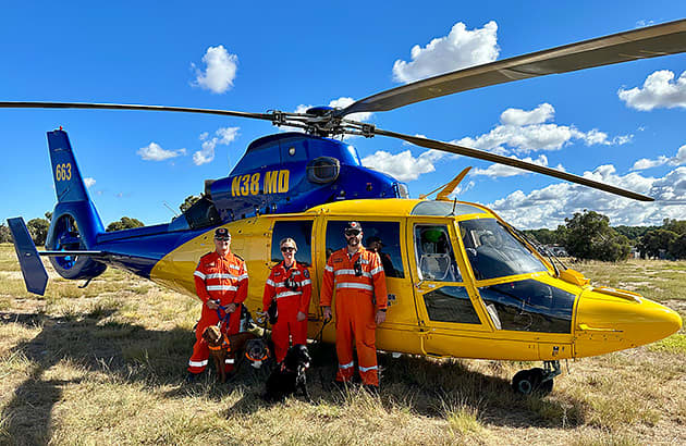 3 search and rescue dogs with their owners standing beside a yellow helicopter
