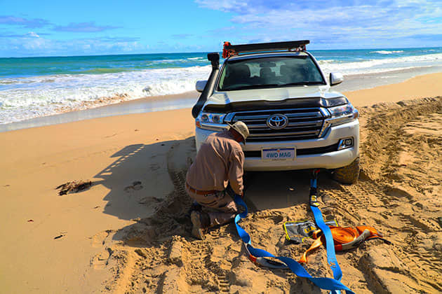 Man attaching straps to the front of a bogged vehicle