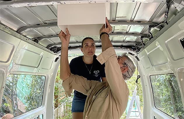 Two people working on a van conversion inside the van
