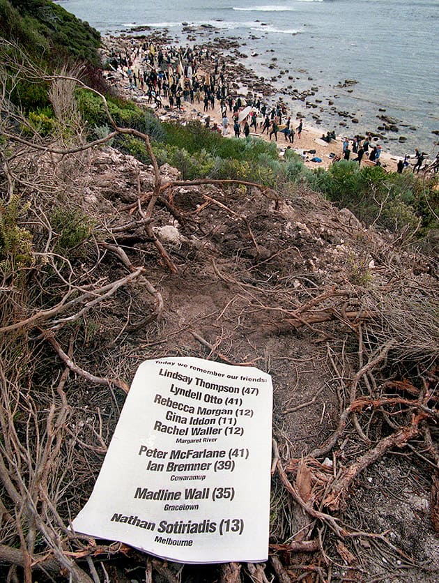 A list of names sits up high on the cliff, with the beach below filled with people.