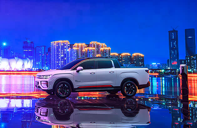 A white Geely Radar parked in front of a cityscape at night