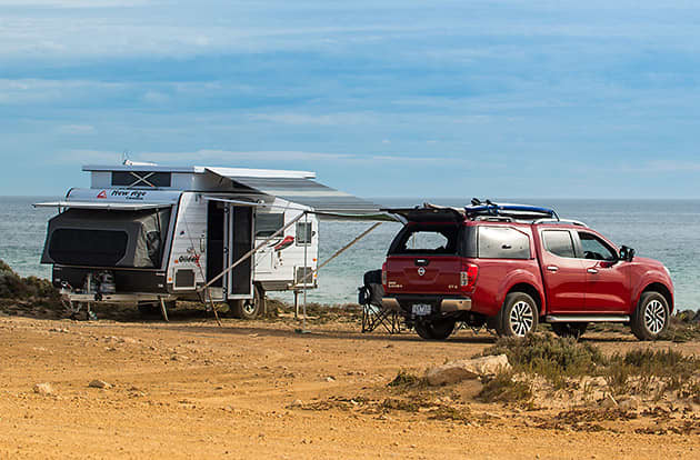A poptop caravan is set up next to a 4 wheel drive near the beach.
