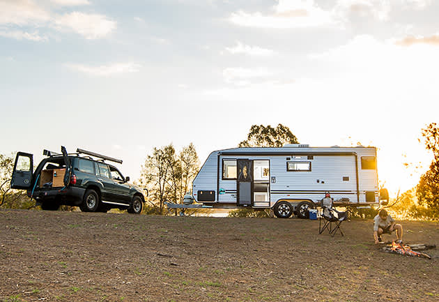 A full-walled caravan is parked near a campfire, with its door open.