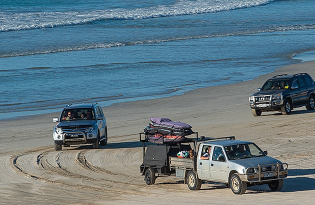 A four-wheel drive pulling a trailer along a beach