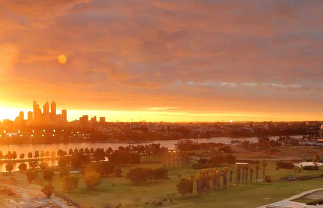 The sun is setting over Burswood Park, with the Perth city skyscrapers in the background