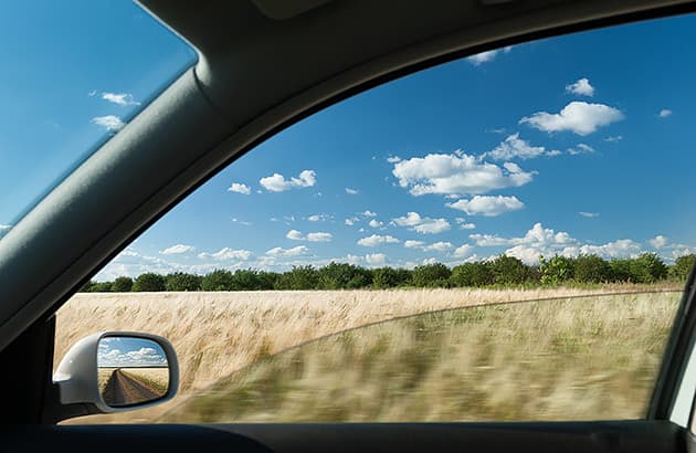 A driver-side car window half open as the car travels in the countryside