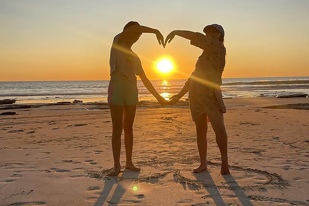 Two girls forming a heart shape with their arms at sunset