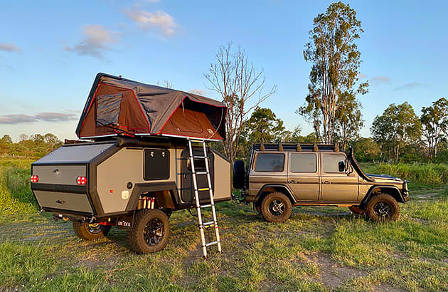 A Bruder teardrop camper with a pop top attached to a four-wheel drive