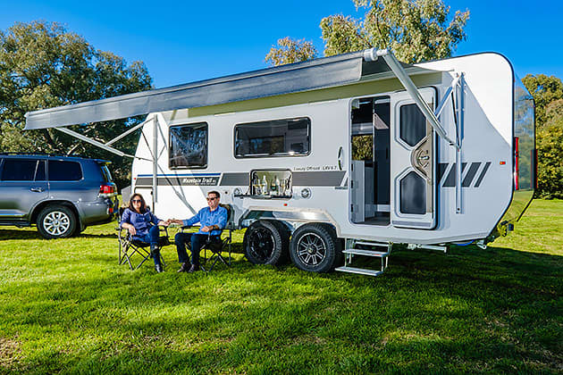Two peple sitting under the awning of a Mountain Trail caravan