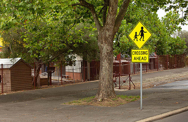 A yellow school zone crossing sign on a suburban street