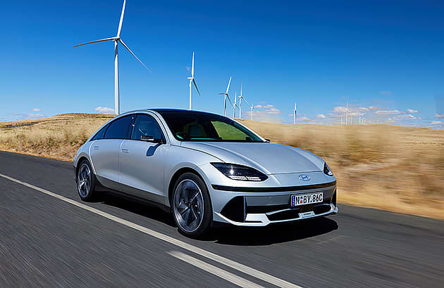 A blue Hyundai Ioniq 6 on a country road with wind turbines in the background