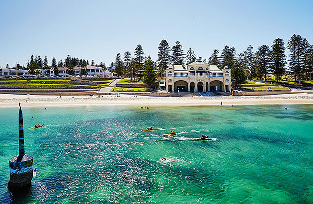 Cottesloe Beach with the water in the foreground and grass terraces and pine trees along the foreshore
