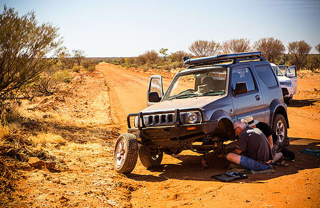 A 4WD with it's front wheel off on a dirt track with two men carrying out repairs
