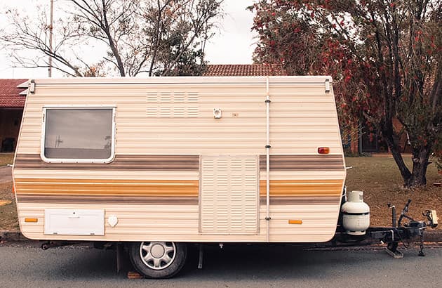 An older style, small caravan parked on the road outside a house