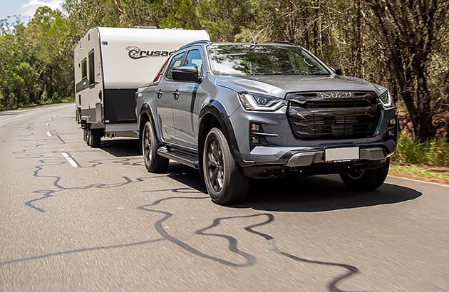 A grey 4WD vehicle towing a caravan on a regional road