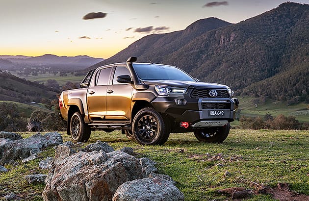 A Toyota Hilux on a green hillside with mountains in the background