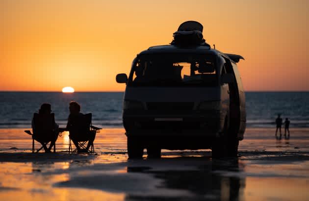 Couple enjoying Cable Beach Broome sunset next to their caravan
