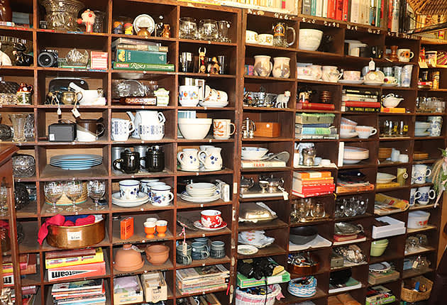 A large wooden shelving unit full of goods inside an op shop