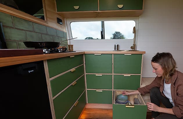 A woman near rows of draws under a benchtop in a campervan