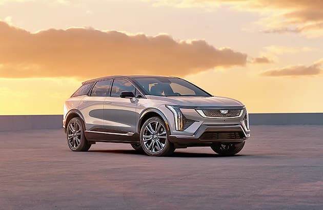 A grey Cadillac Optiq parked on a tarmac at sunset