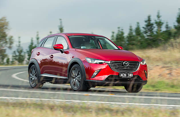 A red Mazda CX-3 driving on a country road.
